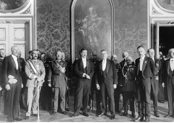Uroczyste spotkanie panów w galowych strojach, w tym wojskowych, przed obrazem. W tle bogata tapeta. bbwr.