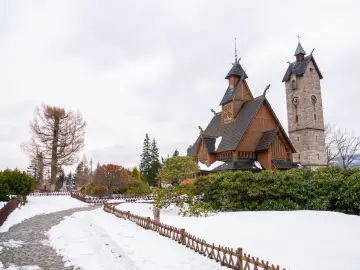 Drewniany kościółek i kamienna wieża zegarowa w zimowej scenerii. To urokliwe miasto u podnóża Śnieżki, gdzie śnieg otula ścieżki i drzewa.