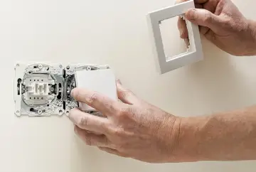 Instrukcja: jak zamontować włącznik światła. Dłonie montują biały włącznik do gniazdka elektrycznego.