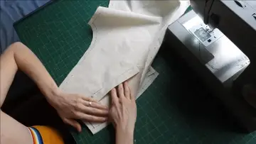 Mains travaillant sur un patron de couture, ajustant un tissu pour une poche raglan, à côté d'une machine à coudre Singer.