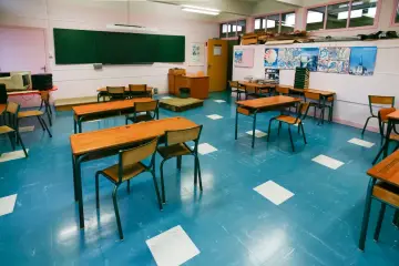 Pusta klasa z niebieską podłogą i drewnianymi ławkami. Nauczyciel zastanawia się, ile wcześniej trzeba zapowiedzieć sprawdzian.