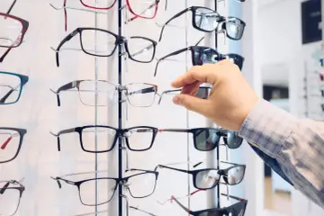 Ręka wybiera okulary z apteki. Wiele oprawek w różnych stylach i kolorach czeka na klientów.