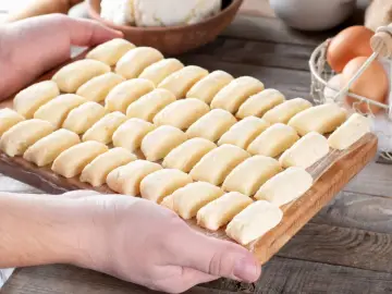 Ania gotuje pierogi leniwe. Na desce leżą rzędy gotowych do gotowania pierogów leniwych, obok jajka i twaróg.