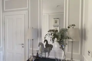 Elegancka sztukateria w przedpokoju podkreśla klasyczny styl. Dwa koniki, lampy i wazon z gałązkami dodają uroku.