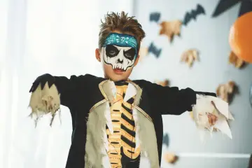 Chłopiec w makijażu czaszki i stroju szkieletu, idealny pomysł na to, jak zrobić strój zombie dla dziecka na Halloween.