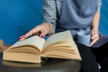 Dłoń z czerwonymi paznokciami dotyka otwartej książki.