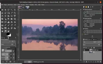 Mglisty poranek nad rzeką, edytowany w **GIMP 2.10**. Widać odbicie drzew w wodzie i wschód słońca.