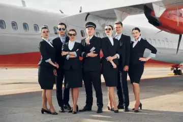 Grupa pilotów i stewardess w eleganckich mundurkach pozuje przed samolotem.