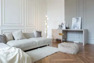Elegancki salon z sofą, dywanem i sztukaterią na ścianach. Panele ścienne dodają wnętrzu klasycznego charakteru.