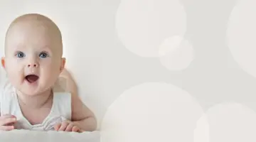 Zaskoczony 4-miesięczne dziecko skok rozwojowy, z szeroko otwartymi ustami i oczami, leży na brzuchu.