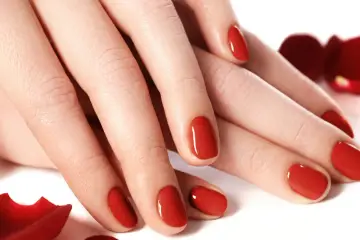 Dłonie z idealnym, czerwonym manicure. Lśniące tytanowe paznokcie, otoczone płatkami czerwonych róż, emanują elegancją i zmysłowością.