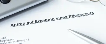 Ein Dokument mit der Überschrift "Antrag auf Erteilung eines Pflegegrads" liegt auf einem Tisch. Daneben liegen ein Stift und eine Brille.