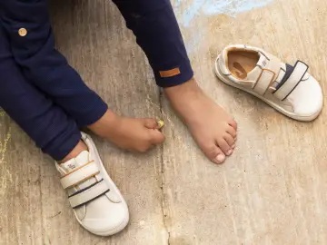 Niño descalzo dibuja con tiza junto a sus zapatos de calzado fisiológico, listos para la aventura.
