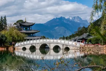 Kamienny most łukowy nad jeziorem, w tle pagody i góry. Chiny ciekawostki, jak z obrazka.