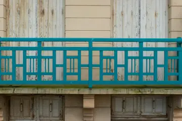 Turkusowe, geometryczne mocowanie balustrady od czoła na tle starych, drewnianych drzwi i jasnej ściany.
