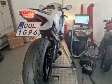 Biały motocykl na hamowni, przygotowany do pomiaru mocy. Widoczna tablica rejestracyjna DOL 1G96. Blokowanie motocykla na A2 to kluczowy etap testów.