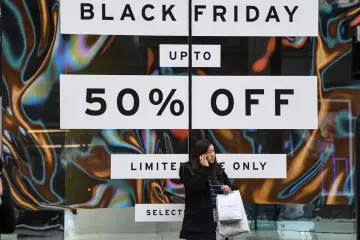 Kobieta z torbami na tle szyldu "Black Friday 50% OFF". Czy to zapowiedź wzrostu cen w koszyku zakupowym przed promocjami?