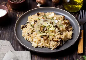 Kremowe risotto z pieczarkami, posypane parmezanem i ziołami, na ciemnym talerzu.
