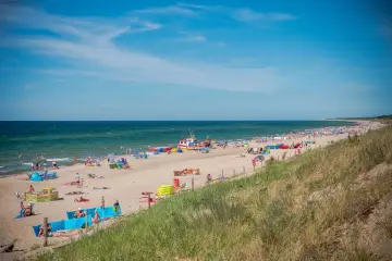 Słoneczna plaża w Dąbkach pełna wypoczywających ludzi i kolorowych parawanów. Warto tu przyjechać na wakacje!