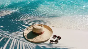 Słomkowy kapelusz i okulary przeciwsłoneczne na piaszczystej plaży, obok turkusowej wody. Idealne miejsce, by pomyśleć, gdzie na wakacje 2026.