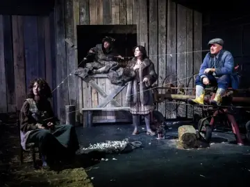 Cztery postacie na scenie, przygotowujące się do teatralnego tournee. Scenografia przypomina wiejską stodołę.