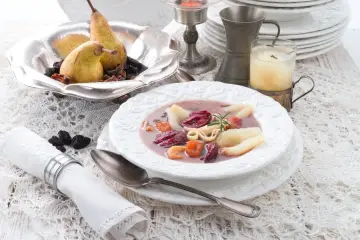 Elegancka czarna polewka z owocami, jak z "Pana Tadeusza", podana na białej zastawie, z gruszkami i śliwkami w tle.