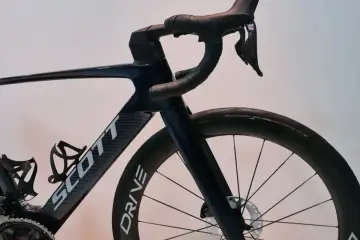 Ciemnoniebieski rower Scott z karbonową ramą i kierownicą. Widoczny mostek, koło z oponą Schwalbe Pro One i hamulec tarczowy.