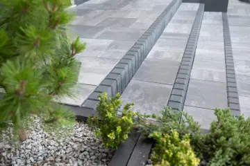 Nowoczesne aranżacje kostka brukowa wzory: szare płyty i obrzeża tworzą elegancką ścieżkę, otoczoną zielenią.
