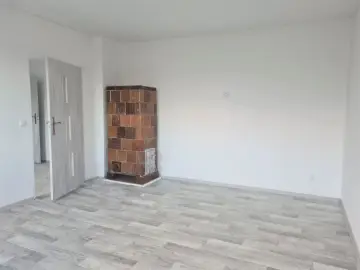 Puste pomieszczenie z piecem kaflowym i drzwiami. To może być przyszłe mieszkanie komunalne po remoncie.