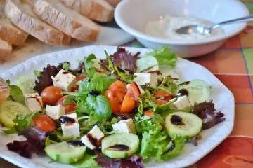 Świeża sałatka z pomidorami, ogórkiem i serem feta, polana aromatycznym sosem truflowym. Obok kromki chleba i miseczka dipu.