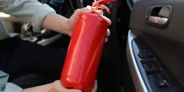 Ręce trzymające czerwoną gaśnicę w samochodzie. Zastanawiasz się, gdzie wyrzucić gaśnicę?