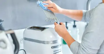 Jak wyczyścić przypalony toster sandwich bez zalewania elektroniki wodą. Ręce czyszczą metalowy ruszt wilgotną ściereczką.