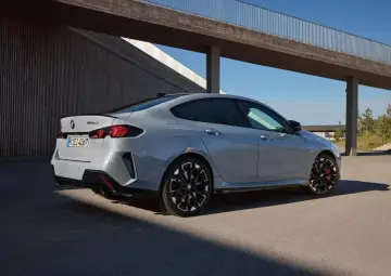 Szare BMW 2 Gran Coupé z czarnymi felgami i czerwonymi zaciskami hamulcowymi stoi na tle nowoczesnej architektury.