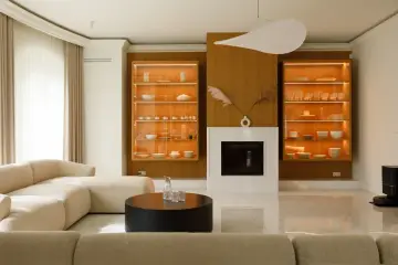 Nowoczesny salon z kominkiem, przeszklonymi witrynami i beżową kanapą.