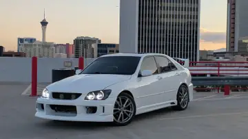Biała Toyota Altezza z tuningiem stoi na parkingu, w tle widać wieżowiec Stratosphere i panoramę miasta o zachodzie słońca.