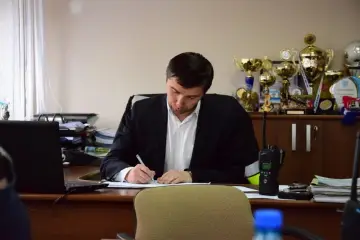 Mężczyzna w garniturze pisze przy biurku, na którym leży laptop i krótkofalówka. Za nim na półce stoją puchary. Zastanawia się, ile trwa kadencja wójta.