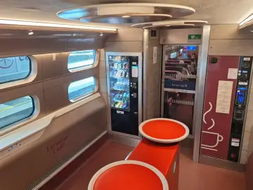 Interior of a Eurostar train from Amsterdam, featuring a cafe area with vending machines, seating, and windows looking out onto the tracks.