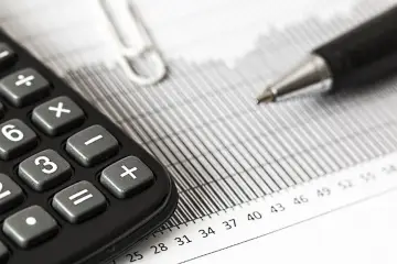 Kalkulator i długopis na dokumentach. Czy podatek od nieruchomości płaci się przelewem podatkowym? Analiza finansowa.