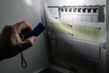 Ręka trzymająca niebieską latarkę oświetla rozdzielnicę elektryczną, pomagając sprawdzić, gdzie jest awaria prądu.