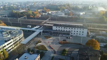 Widok na nowoczesny dworzec PKP Lubliniec z parkingiem wielopoziomowym i torami kolejowymi w tle.