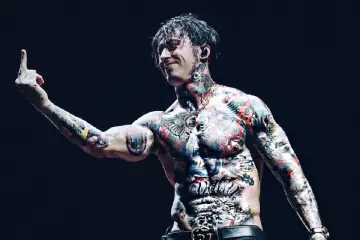 Le chanteur de Falling In Reverse, Ronnie Radke, torse nu et couvert de tatouages colorés, lève le majeur sur scène.