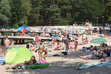 Tłoczna plaża nad jednym z **jezior blisko Wrocławia**. Ludzie opalają się, kąpią i odpoczywają na piasku.
