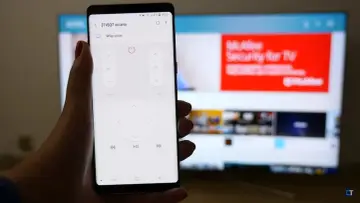 Smartfon z aplikacją do sterowania telewizorem, umożliwiający screen mirroring. Na ekranie telefonu widać przyciski pilota, a w tle telewizor z wyświetloną stroną internetową.