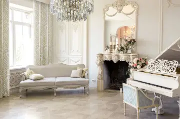 Elegancki salon w stylu wiktoriańskim: kanapa, kominek z lustrem, biały fortepian i kryształowy żyrandol tworzą luksusową atmosferę.