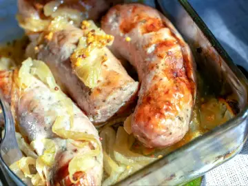 Pieczona biała kiełbasa surowa z cebulą i musztardą w naczyniu żaroodpornym.