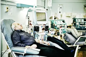 Starszy mężczyzna odpoczywa podczas zabiegu hemodializy, podłączony do aparatury medycznej.