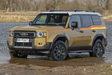 Złoty Land Cruiser 100 z kolorowymi pasami na boku, stojący w wodzie.
