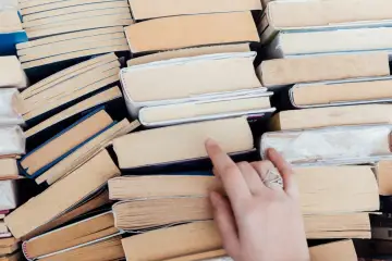 Stos książek, wśród nich lektury klasa 8. Dłoń sięga po jedną z nich, by rozpocząć czytanie.