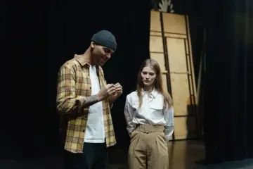 Mężczyzna w czapce i koszuli w kratę rozmawia z kobietą na scenie. Stoją blisko siebie, przygotowując się do występu.