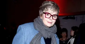 Karolina Korwin Piotrowska w okularach i niebieskim płaszczu, z szarym szalem na szyi.